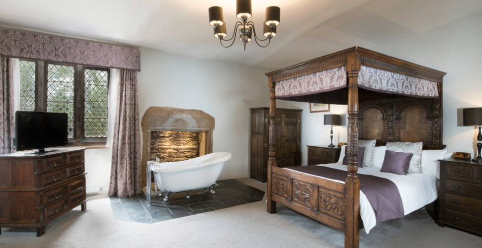 A room with a four poster bed on the right, a bath in the middle and a TV on the left at Boringdon Hall Hotel and Spa 